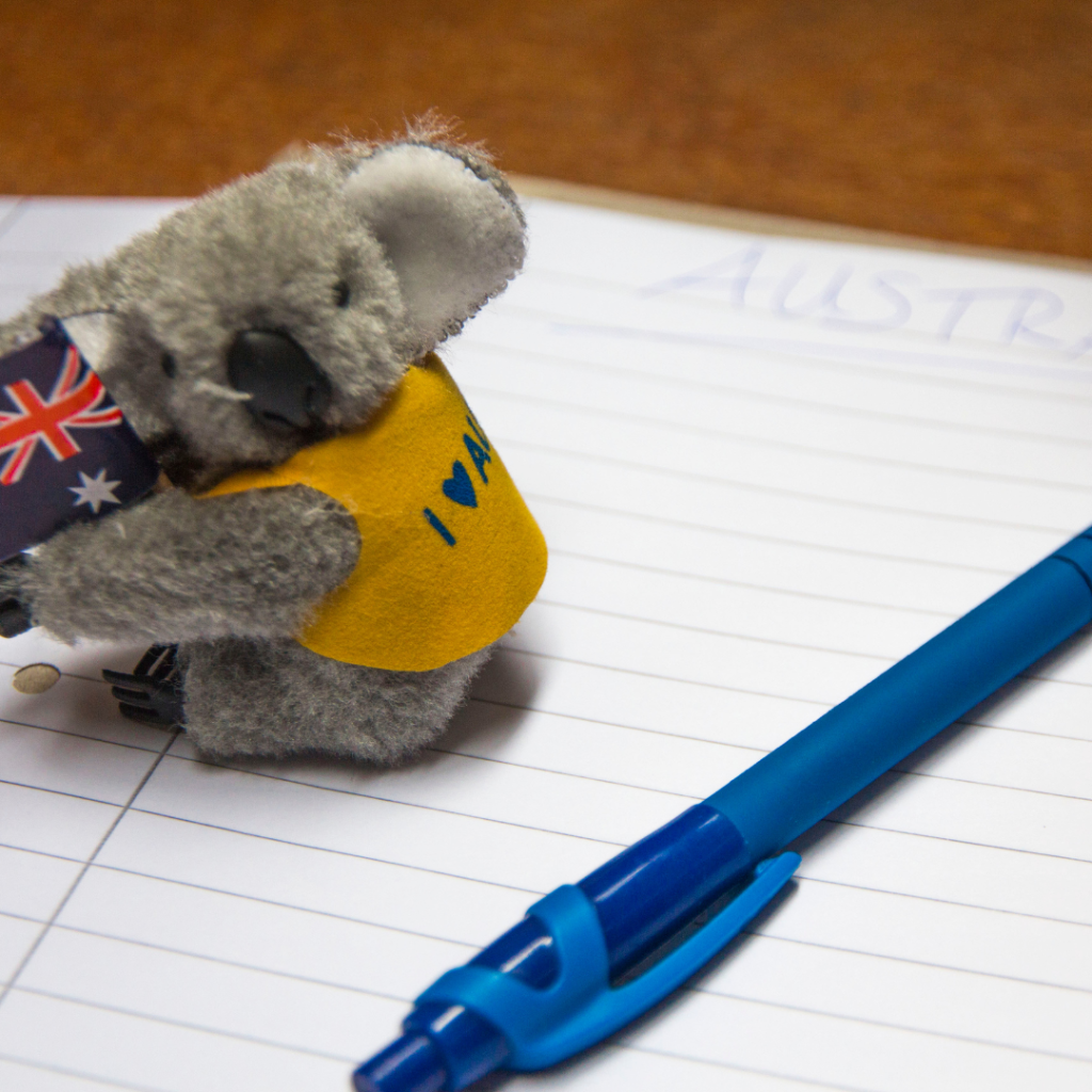 Government Merchandise Australian Koala Welcome Gift – Government Visitor & Community Pack Ideas Small koala holding an Australian flag next to a blue pen on a notebook.