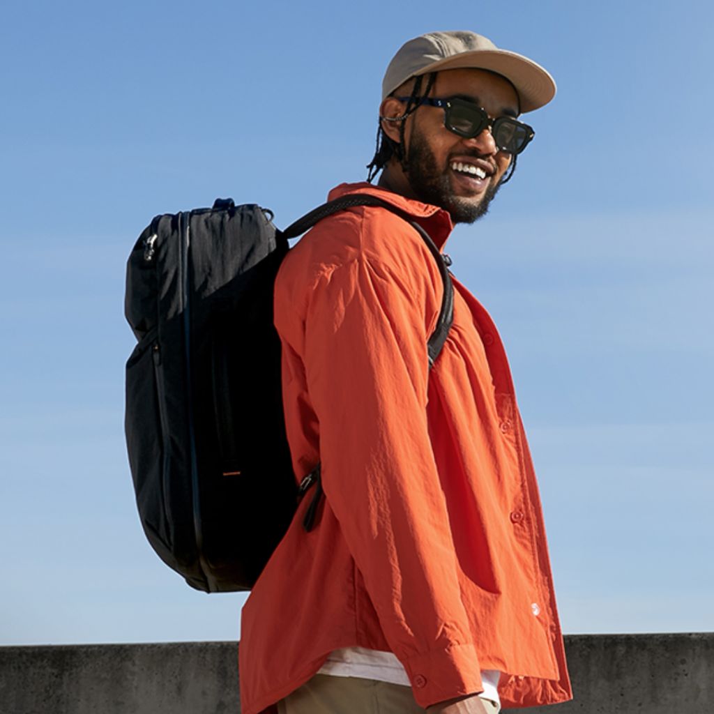Government Field Staff Backpack – Durable Day Pack for Australian Programs Man in orange shirt wearing a black backpack outdoors under blue Australian sky.