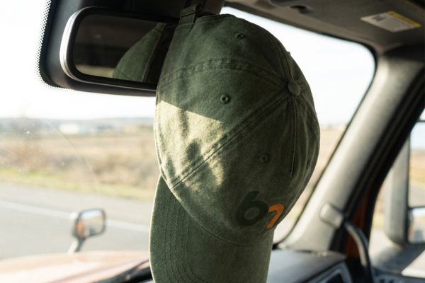 Green branded promotional cap hanging inside a vehicle, showing wearable merchandise that keeps a business visible in everyday settings and supports customer referrals.