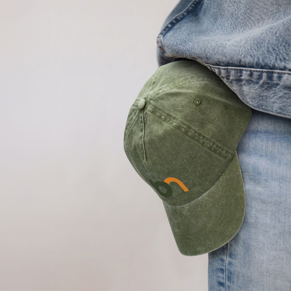 Branded Promotional Cap for Everyday Brand Visibility Green branded promotional cap held by a person in casual clothing, showing wearable merchandise that creates ongoing brand exposure and supports customer referrals.