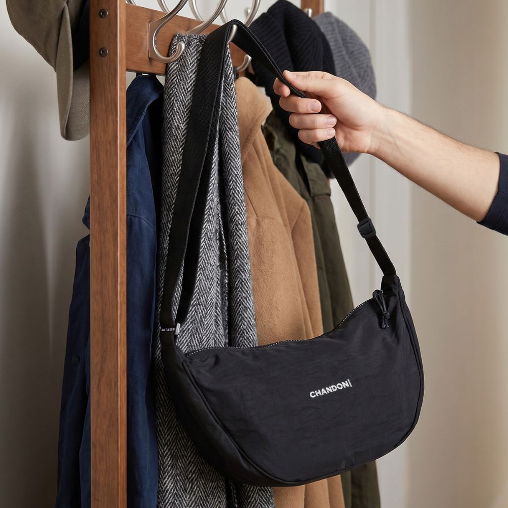 Branded Shoulder Bag for Customer Gifting Black branded shoulder bag being picked up from a coat rack, showing useful promotional merchandise that keeps a brand visible and supports customer referrals.