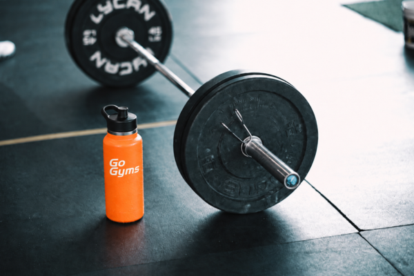 Orange Go Gyms branded drink bottle beside a barbell and weight plates on a gym floor, showcasing promotional gym merchandise for Australian fitness centres.